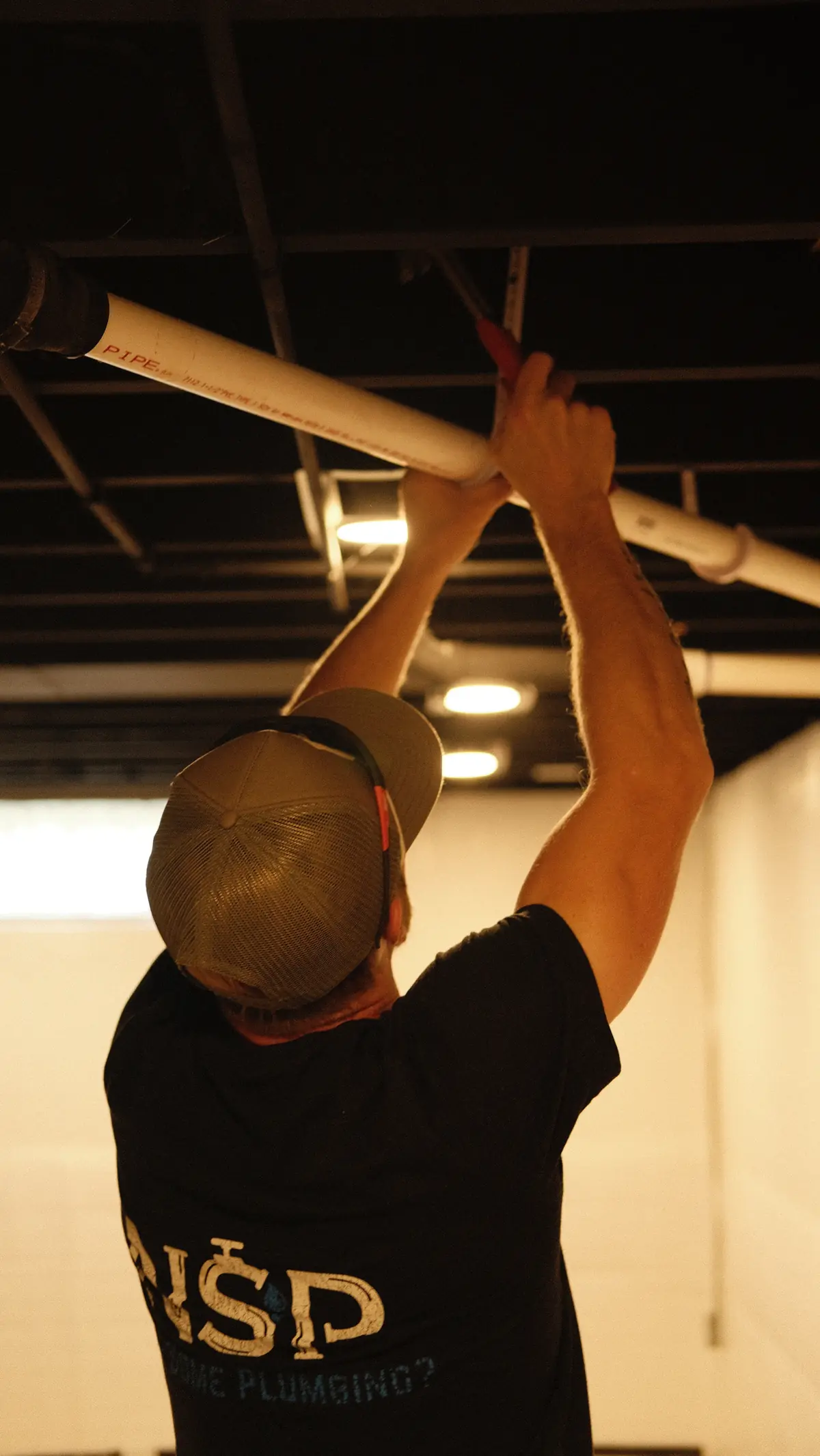 NSP Plumbing plumber hanging new PVC drain pipe from a basement ceiling