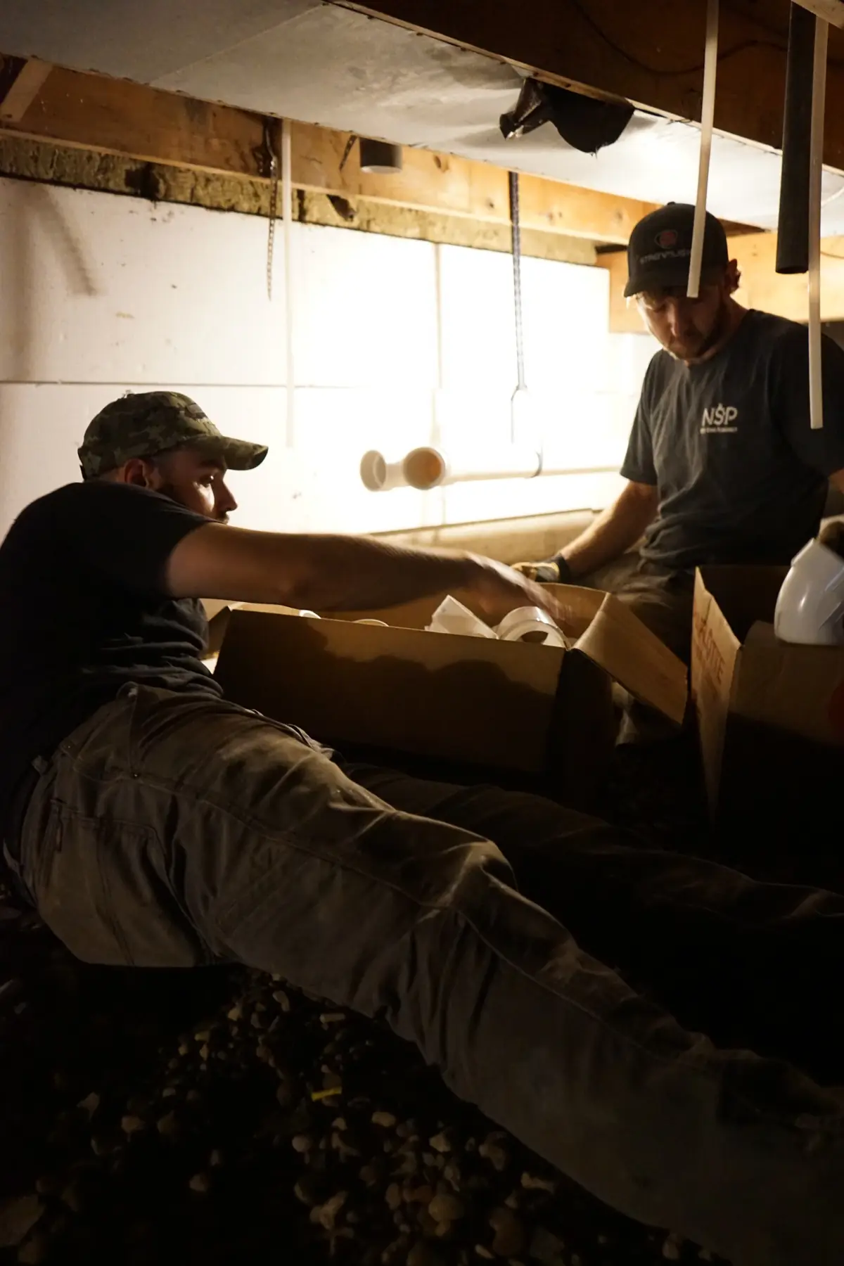 NSP Plumbing crew unpacking PVC fittings in a crawlspace during a repipe